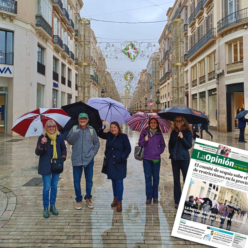 Senior student group smiling on a commercial street in rainy Malaga. Same photo is overlayed on the cover page of a newspaper. 